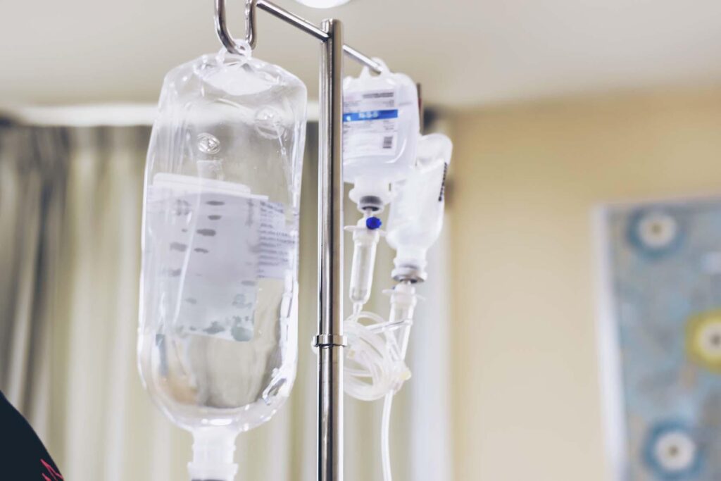 Close-up view of intravenous (IV) therapy bags hanging on a metal stand in a clinical setting.