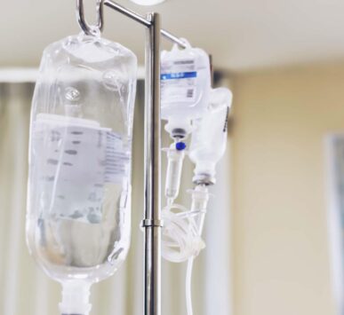 Close-up view of intravenous (IV) therapy bags hanging on a metal stand in a clinical setting.
