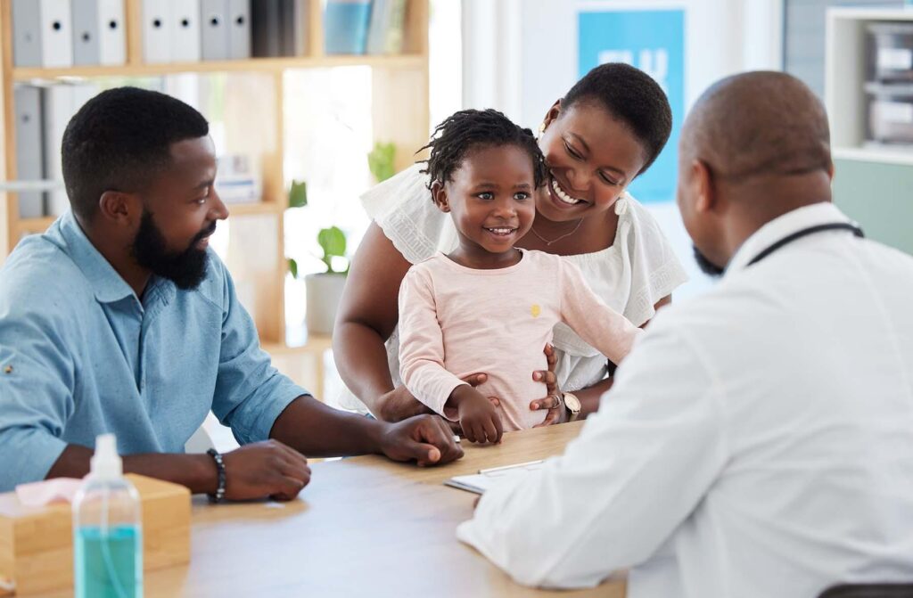 A smiling Black family with a young daughter at a medical consultation with a doctor.