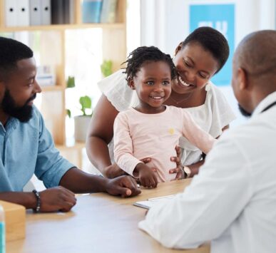 A smiling Black family with a young daughter at a medical consultation with a doctor.
