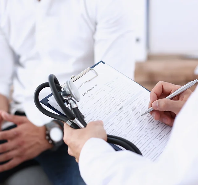 A healthcare provider holds a clipboard and stethoscope, filling out a patient’s medical history form during a consultation.