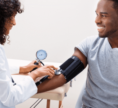 A smiling man has his blood pressure checked by a healthcare provider during a routine preventive care visit.