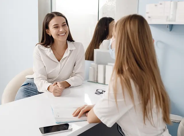 A smiling woman speaks with a healthcare professional during a consultation in a bright, modern clinic.